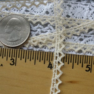 May include: A close-up of a white crocheted lace trim with a scalloped edge. The lace is measured against a ruler, showing it is approximately 3/8 inch wide.