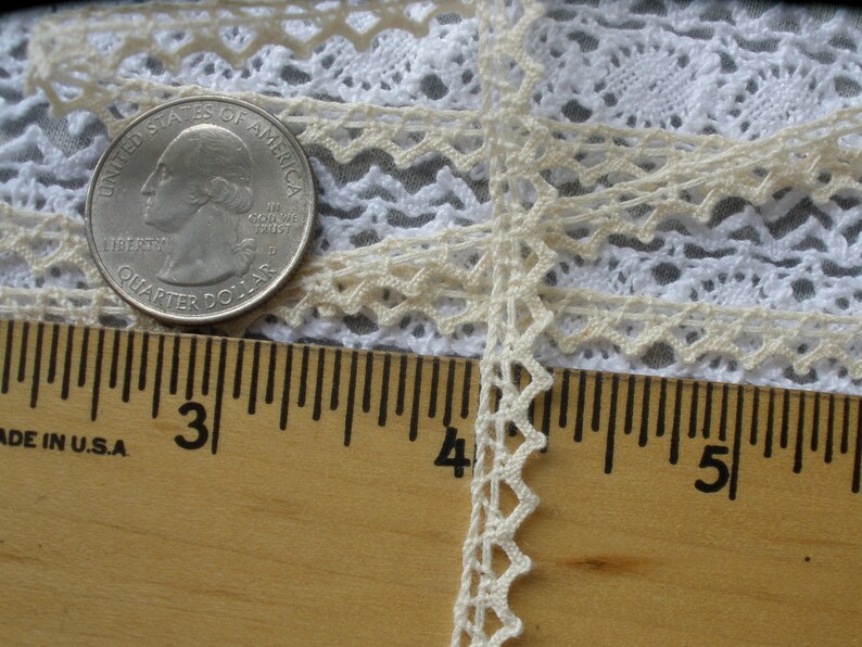 May include: A close-up of a white crocheted lace trim with a scalloped edge. The lace is measured against a ruler, showing it is approximately 3/8 inch wide.