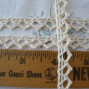 May include: White crochet trim with a scalloped edge, measured against a wooden ruler with the words "Mother Goose Shoes" printed on it.