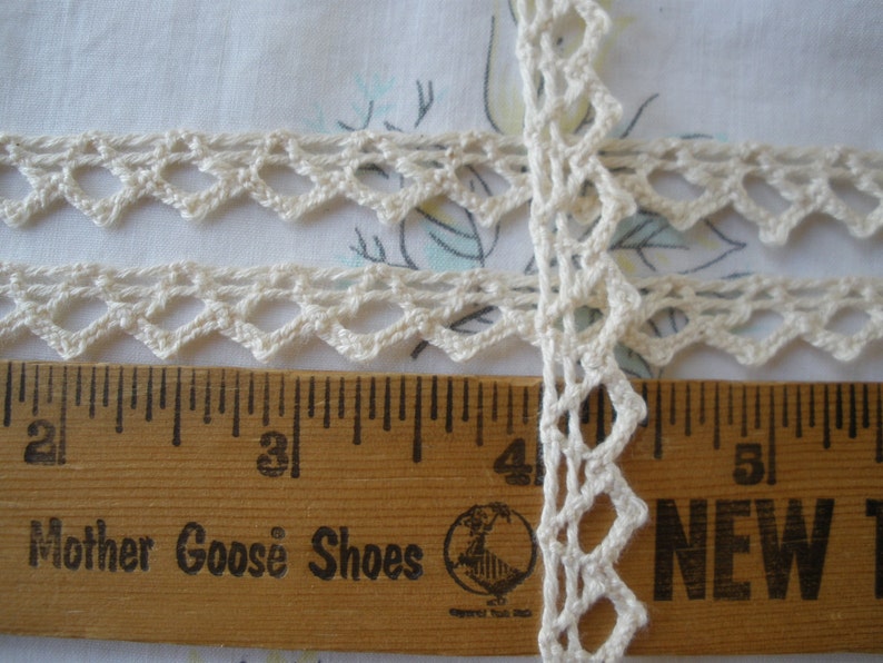 May include: White crochet trim with a scalloped edge, measured against a wooden ruler with the words "Mother Goose Shoes" printed on it.