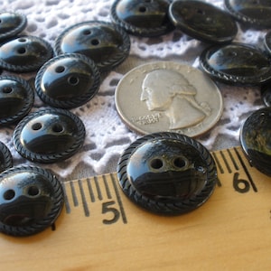May include: A collection of black plastic buttons with a raised, rope-like design around the edge. The buttons have two holes and are approximately 1 inch in diameter.