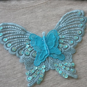 May include: A light blue butterfly applique with sequins, perfect for adding a touch of whimsy to clothing or crafts.