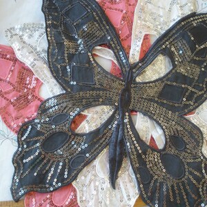 May include: Three sequined butterfly appliques in pink, white, and black. The black butterfly is the largest and has a more detailed design.
