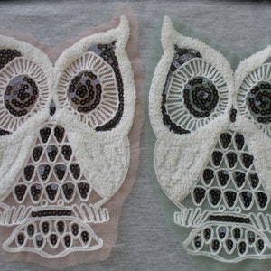 May include: Two white owl-shaped fabric patches with black sequins. The owl on the left is on a pink background and the owl on the right is on a green background.