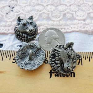 May include: Three silver metal buttons with wolf head designs. The buttons are approximately 1 inch in diameter. The buttons are on a wooden ruler with inch markings.