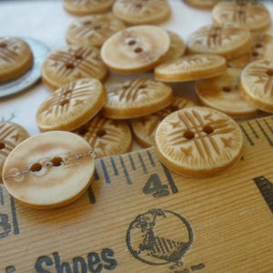 Puede incluir: Una colecci&oacute;n de botones beige y marrones con un dise&ntilde;o decorativo. Los botones est&aacute;n dispuestos sobre una regla de madera con las palabras "Shoes" y "New" visibles.