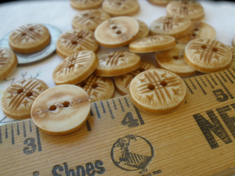 Puede incluir: Una colecci&oacute;n de botones beige y marrones con un dise&ntilde;o decorativo. Los botones est&aacute;n dispuestos sobre una regla de madera con las palabras "Shoes" y "New" visibles.