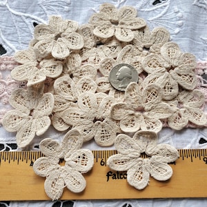 May include: A pile of 15 off-white crocheted flower embellishments, each about 2 inches in diameter, with a hole in the center. A US quarter is included for scale.