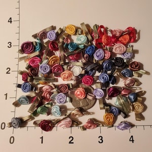 May include: A large assortment of colorful satin ribbon rosettes in various shades of pink, purple, blue, green, red, and brown. The rosettes are approximately 1/2 inch in diameter and are perfect for adding a touch of elegance to crafts, scrapbooking, and other projects.
