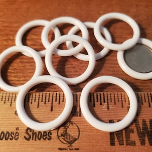 May include: A close-up of ten white plastic rings, some stacked on top of each other. The rings are about 1 inch in diameter. A ruler is visible in the background.