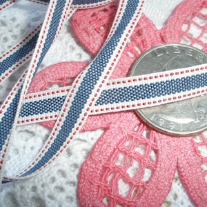 May include: Close-up of a blue, white, and red striped ribbon. The ribbon is approximately 0.5 inches wide and is lying on a pink floral lace design. A US quarter is also in the image.