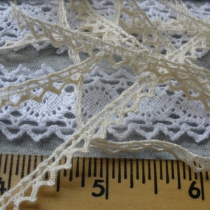 May include: Two pieces of white lace trim with a scalloped edge. The lace is laid out on a wooden ruler with markings for inches. The ruler shows the numbers 4, 5, and 6.