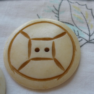 May include: A white button with a brown geometric design. The button has two holes in the center.