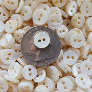 May include: A close-up of a pile of white, two-hole, mother-of-pearl buttons. A US quarter is included for scale.