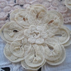 May include: A delicate, off-white crocheted flower with a layered design. The flower is made of a soft, lightweight fabric and has a delicate, feminine look.