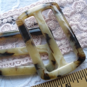 May include: Two brown and white marbled plastic belt buckles. The buckles are rectangular with two slots for a belt.