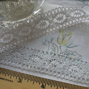 May include: Silver metallic lace trim with a delicate floral pattern. The lace is approximately 1 inch wide and has a shimmery finish.