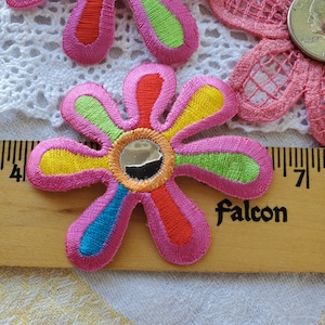 May include: Pink flower-shaped fabric patch with a mirrored center. The flower has six petals with alternating stripes of yellow, green, red, and blue.