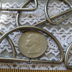 May include: A close-up of a silver metal D-ring, with a US quarter for scale. The D-ring is about 2 inches in diameter.