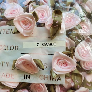 May include: A close-up of a bag of pink and green fabric rose embellishments. The label reads "71 CAMEO".