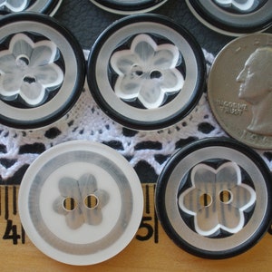 May include: A close-up of a group of black and white buttons with a flower design. The buttons are about 1 inch in diameter and have a raised flower design in the center. The buttons are surrounded by a black border and a white ring.