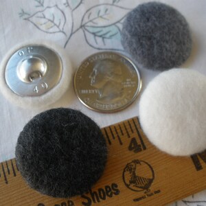 May include: Four buttons, two black, one white, and one silver with a white border. The buttons are round and have a fuzzy texture. The silver button has the letters "GF" and the number "40" printed on it.