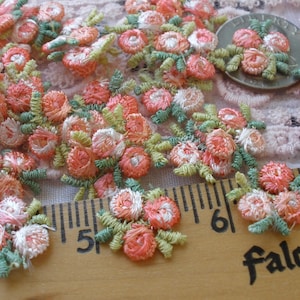 May include: Embroidered floral appliques in shades of peach, pink, and white with green leaves. The appliques are arranged on a light pink lace background. A wooden ruler with the word "Falcon" is in the image.