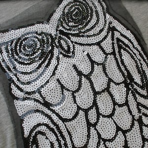 May include: A black and white owl design made of sequins on a gray fabric background.