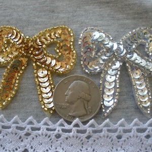May include: Two sequined bows, one gold and one silver, are displayed on a gray fabric background. A US quarter is included for size reference.