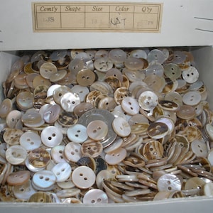 May include: A box filled with 650 natural colored, two-hole, round shell buttons. The buttons are in various shades of brown and white.