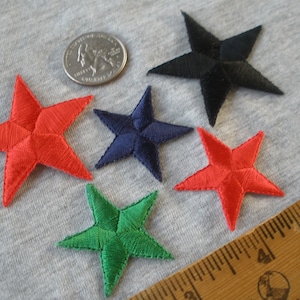 May include: Five embroidered iron-on patches in the shape of stars. The stars are red, green, blue, and black. The patches are approximately 1 inch in diameter.