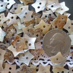 May include: A collection of brown and white iridescent star-shaped buttons made from mother of pearl. The buttons are approximately the size of a US quarter.
