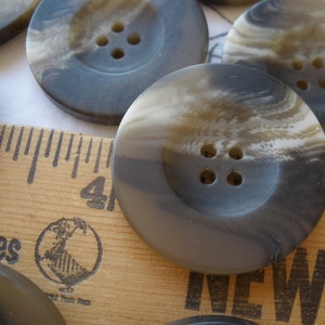 May include: Four-hole black and white swirl buttons with a matte finish. The buttons are on a wooden ruler with the words "Shoes" and "New" printed on it.