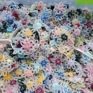 May include: A close-up image of a large collection of colorful beaded flower embellishments. The flowers are made of various colors of beads and fabric, and they are arranged in a random pattern. The flowers are all about 1 inch in diameter.