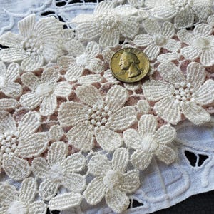May include: Close-up of cream-colored floral lace fabric with a quarter coin for size reference. The lace features detailed, raised flower patterns. The coin shows the profile of George Washington and the year 1935.
