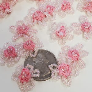 May include: Close-up of several small, pink fabric flowers with a beaded petal design. Each flower has a small, pink fabric rose in the center. A US quarter is included for size reference.