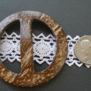 May include: A brown and beige coconut shell belt buckle with a smooth, polished finish. The buckle is shaped like a circle with a center bar.