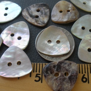 May include: A collection of 12 two-hole iridescent mother of pearl triangle buttons. The buttons are approximately 1 inch in size and have a white, iridescent finish. The buttons are arranged on a brown surface with a ruler for scale.