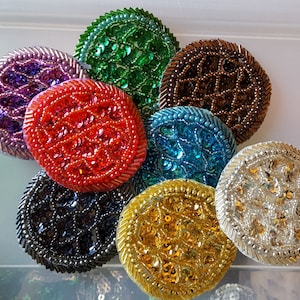 May include: Eight round, decorative, beaded embellishments in various colors, including red, green, blue, gold, silver, purple, brown, and black. The embellishments are made of sequins and beads.