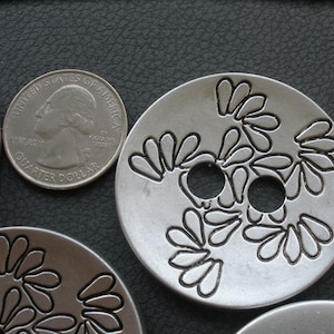 May include: Three silver metal buttons with a floral design. The buttons have two holes each and are approximately 1 inch in diameter.