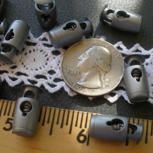 May include: A close-up of silver toggle clasps, some are laying on a white crocheted lace fabric, others are on a wooden ruler with inch markings, and one is next to a US quarter.