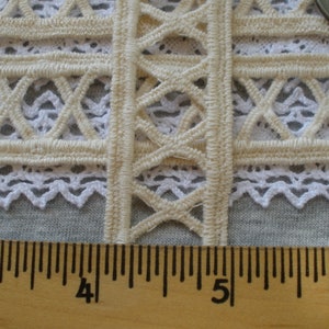 May include: Close-up of a beige crocheted lace trim with a diamond pattern. The trim is measured against a wooden ruler with markings from 3 to 6 inches.