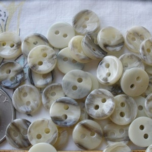 May include: A collection of 2-hole buttons with a mottled, marbled pattern in shades of cream and gray. The buttons are made of a smooth, polished material.
