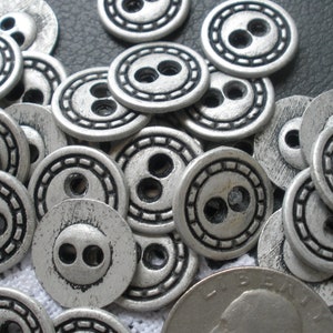 May include: A pile of silver-toned buttons with two holes each. The buttons have a decorative border and a slightly distressed finish.