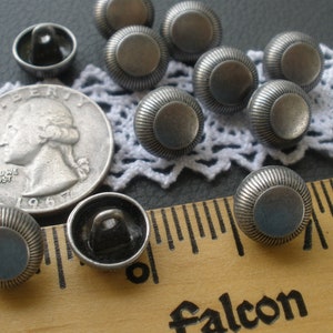 May include: A collection of 10 silver metal buttons with a raised, textured design. The buttons are approximately 1 inch in diameter and have a flat back.