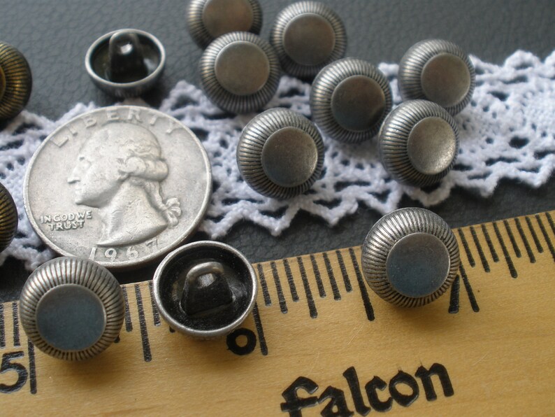 May include: A collection of 10 silver metal buttons with a raised, textured design. The buttons are approximately 1 inch in diameter and have a flat back.