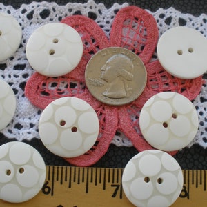 May include: A collection of white plastic buttons with a raised circle pattern. The buttons have two holes and are approximately the size of a US quarter.