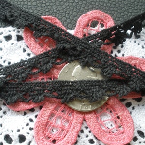 May include: Black crochet lace trim with a scalloped edge. The lace is shown on top of a pink and white crocheted fabric.