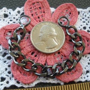 May include: Black metal chain with two jump rings. The chain is about the size of a quarter.