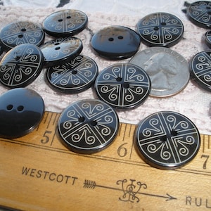 May include: A collection of black buttons with a decorative white design. The buttons are round and oval, with two or four holes. A ruler shows measurements in inches.